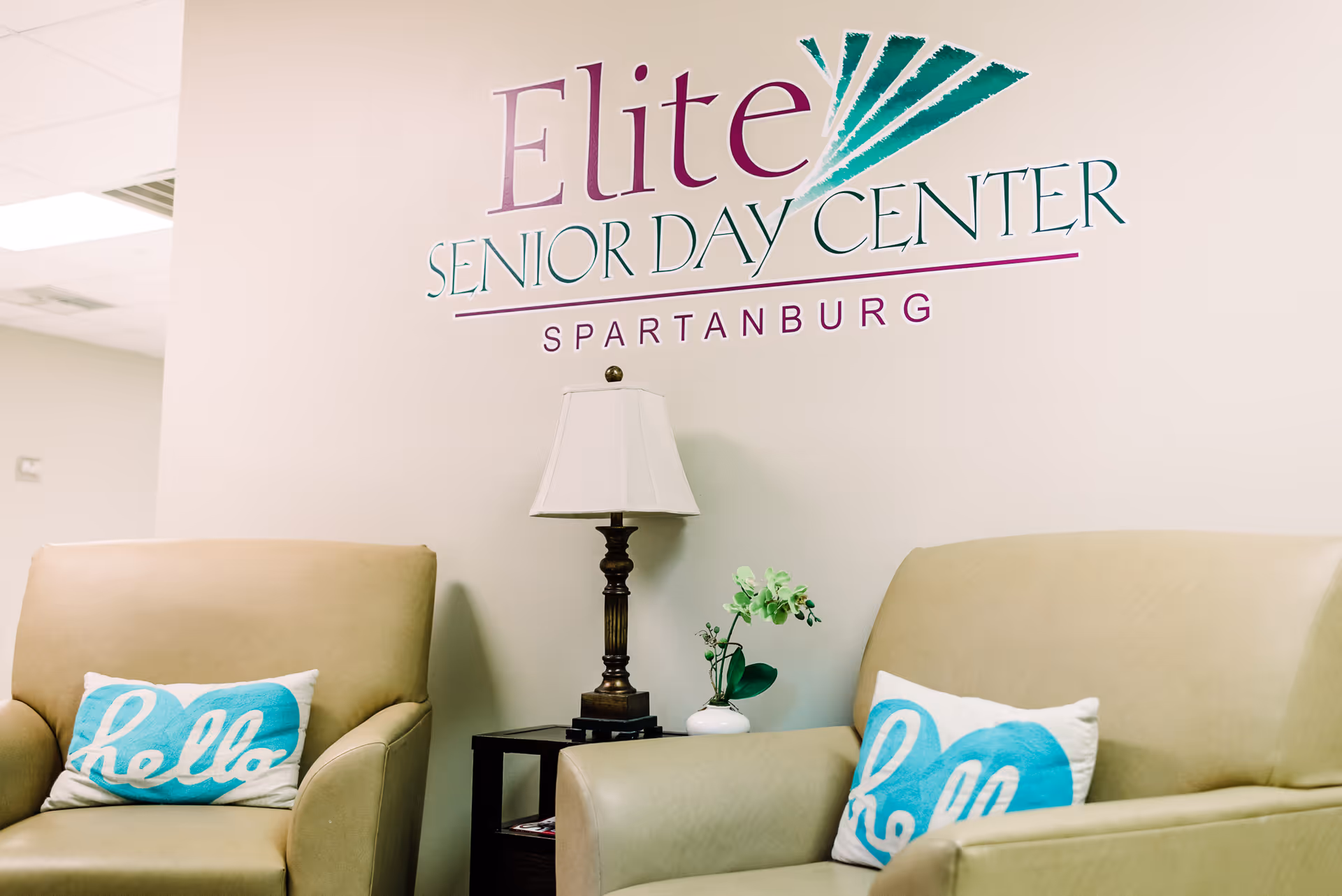 Lobby seating area with beige chairs, lamp, and Elite Senior Day Center sign on wall.