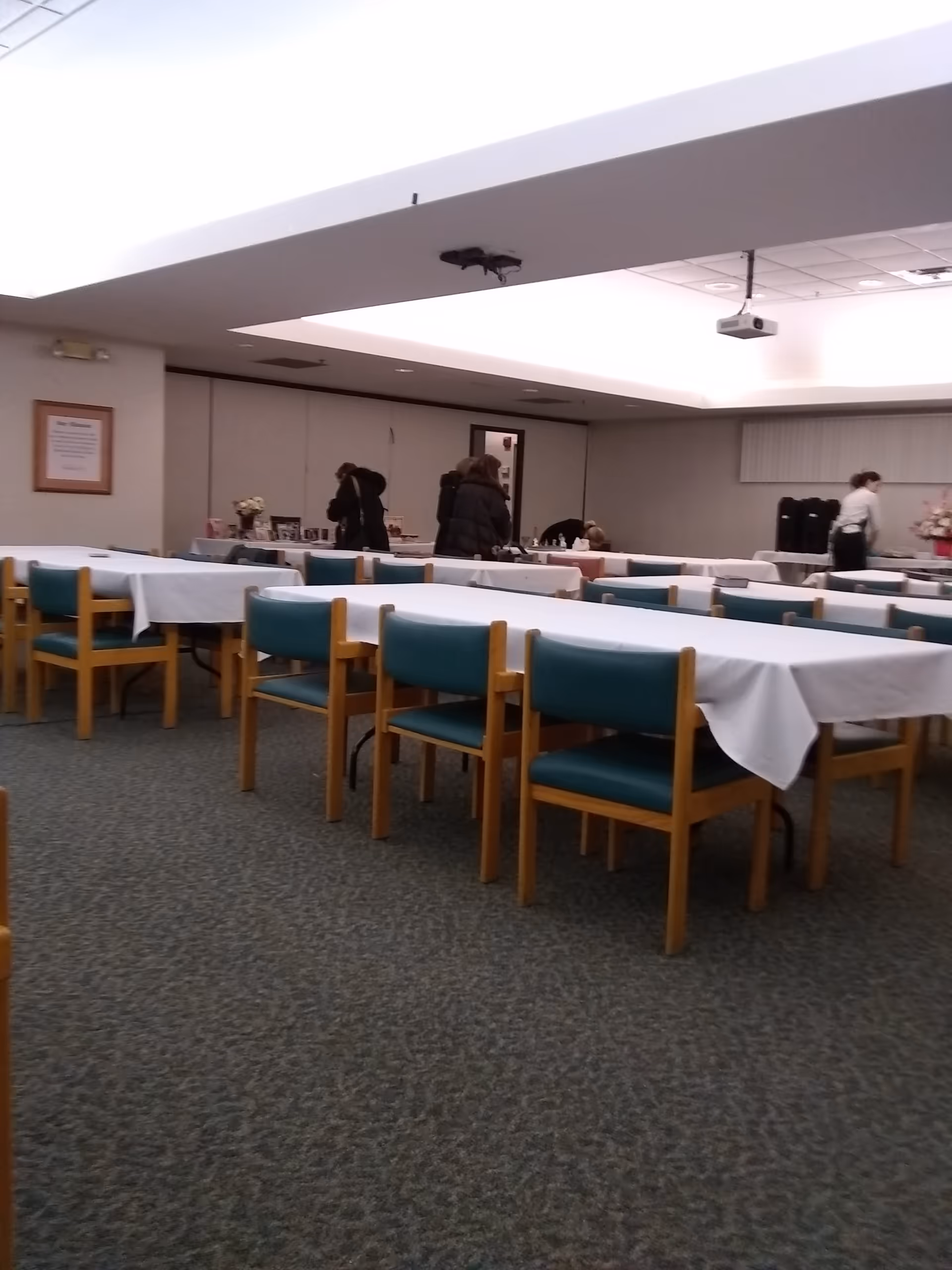 Rows of tables with white cloths and teal chairs in a senior living dining room.