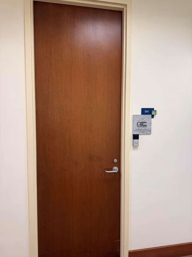 A closed wooden door in a cream hallway with Right at Home signage beside it.