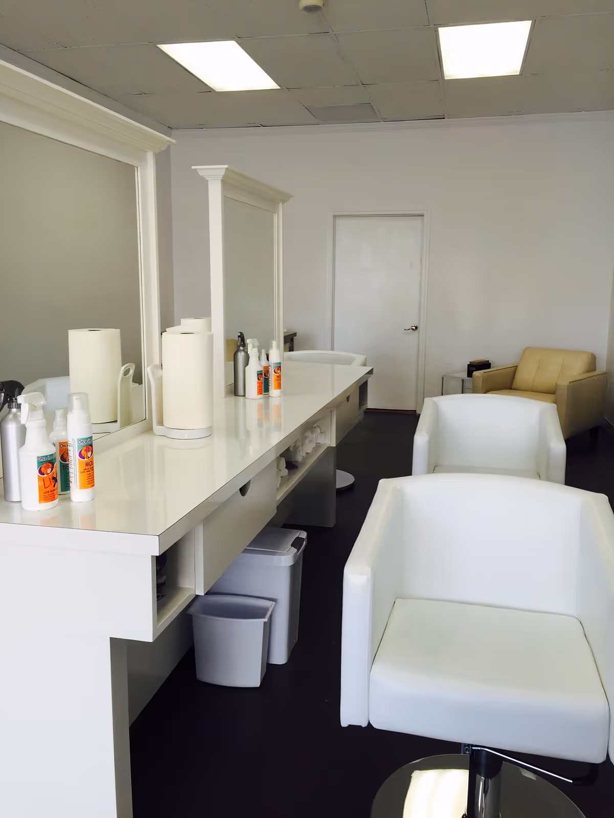 Bright white salon area with mirrors, chairs, and a long counter lined with bottles.