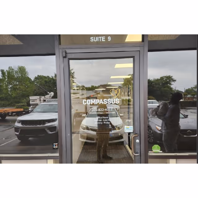 Glass door entrance with Compassus branding and parked cars outside.
