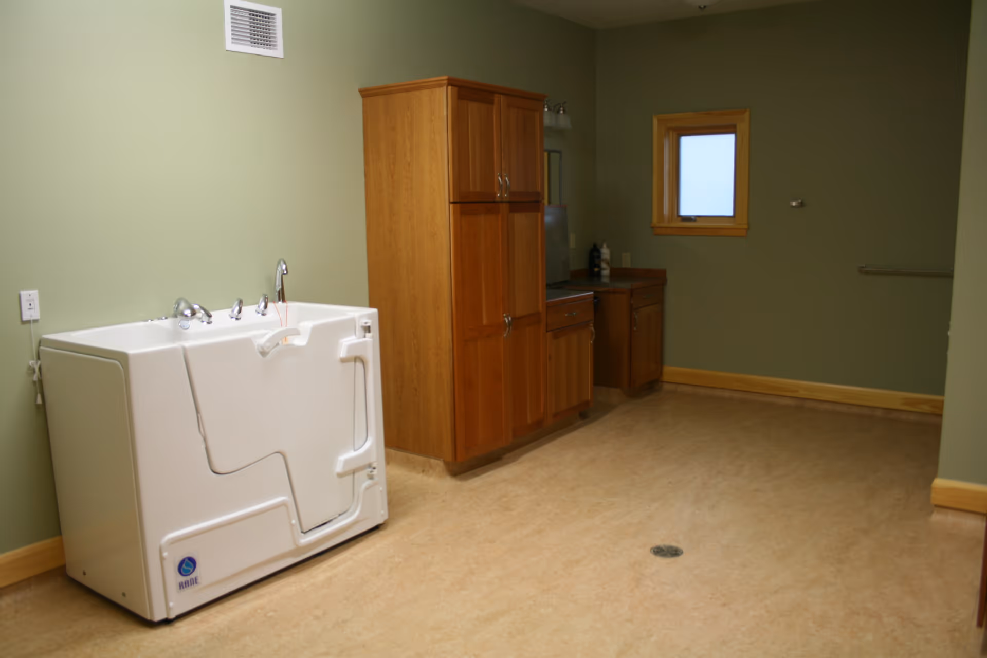 Utility room with a large white appliance, wooden cabinets, sink, and a window.
