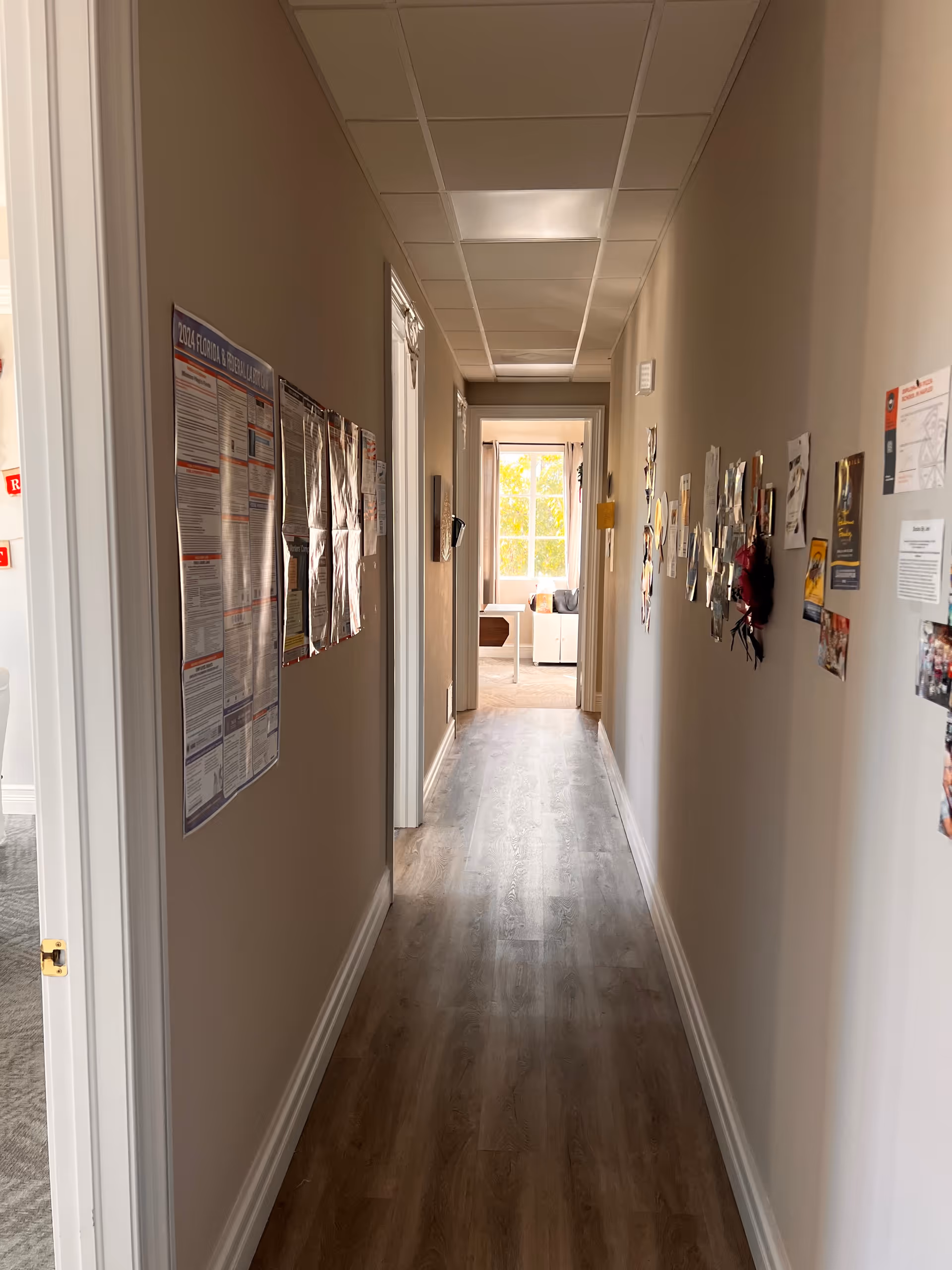 A long hallway in a senior living facility with wall postings leading to a bright room.