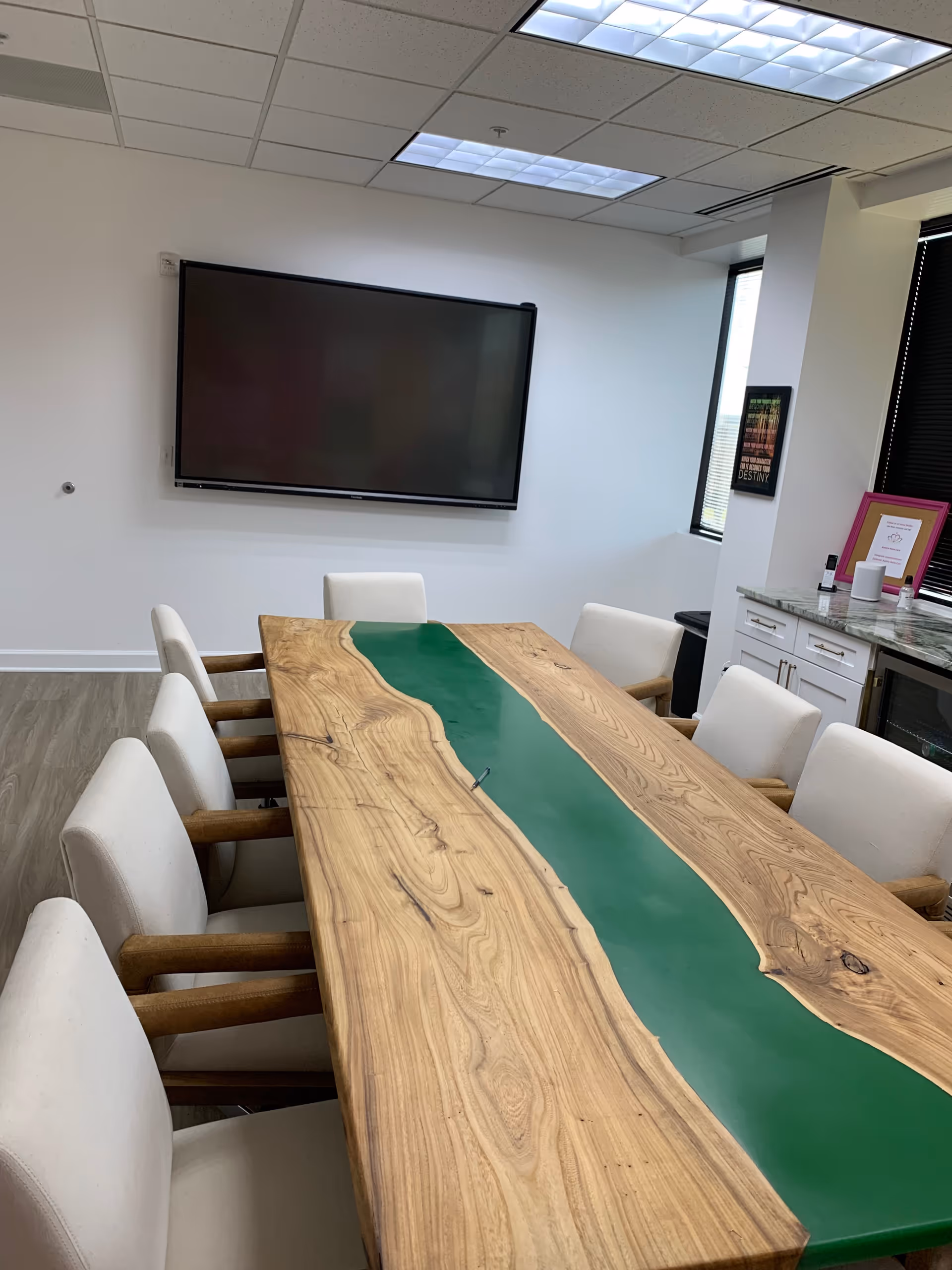 Long wooden conference table with a green stripe, surrounded by beige chairs in a bright room.