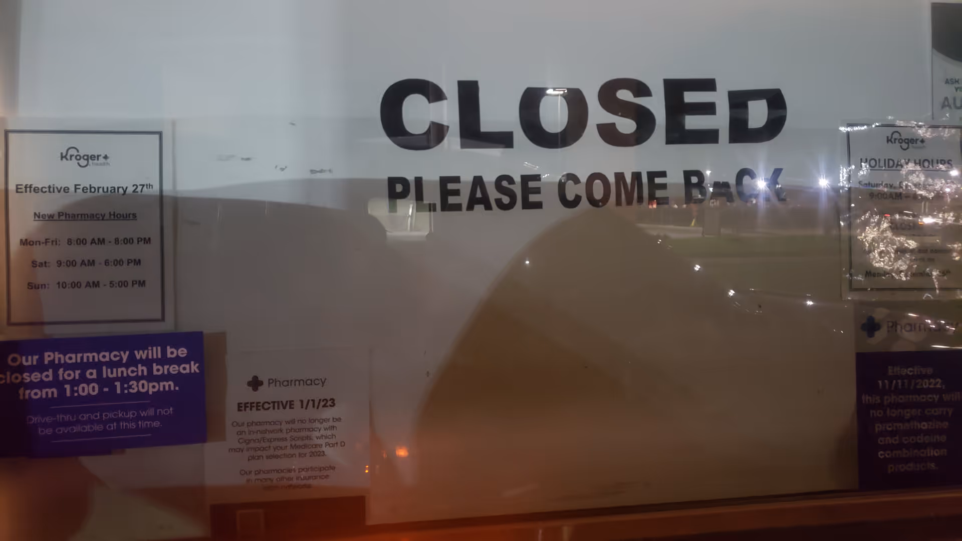 Large 'CLOSED' sign on glass door with notices for Kroger Pharmacy.