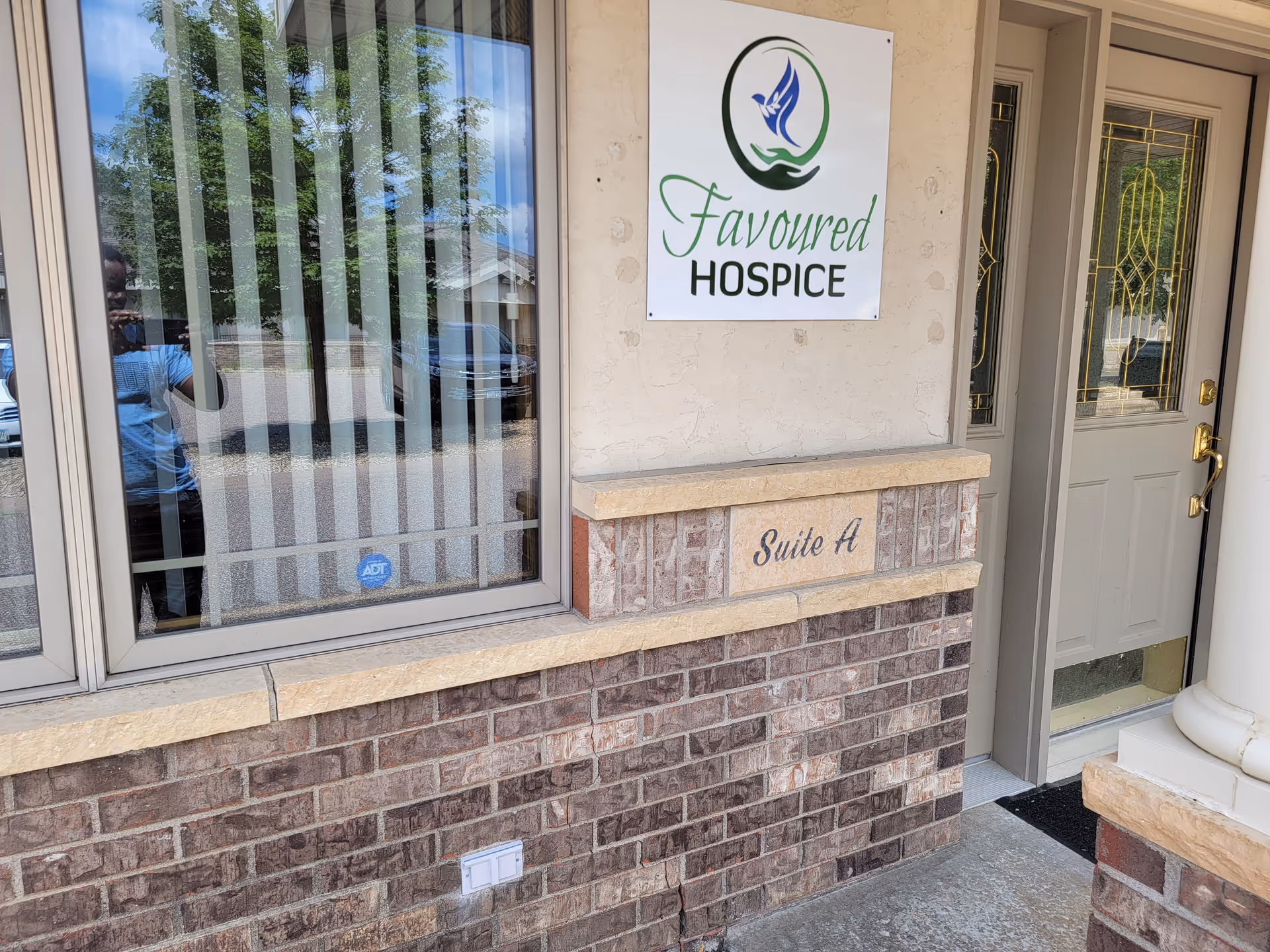 Exterior view of Favoured Hospice entrance with sign, window, and brick façade.