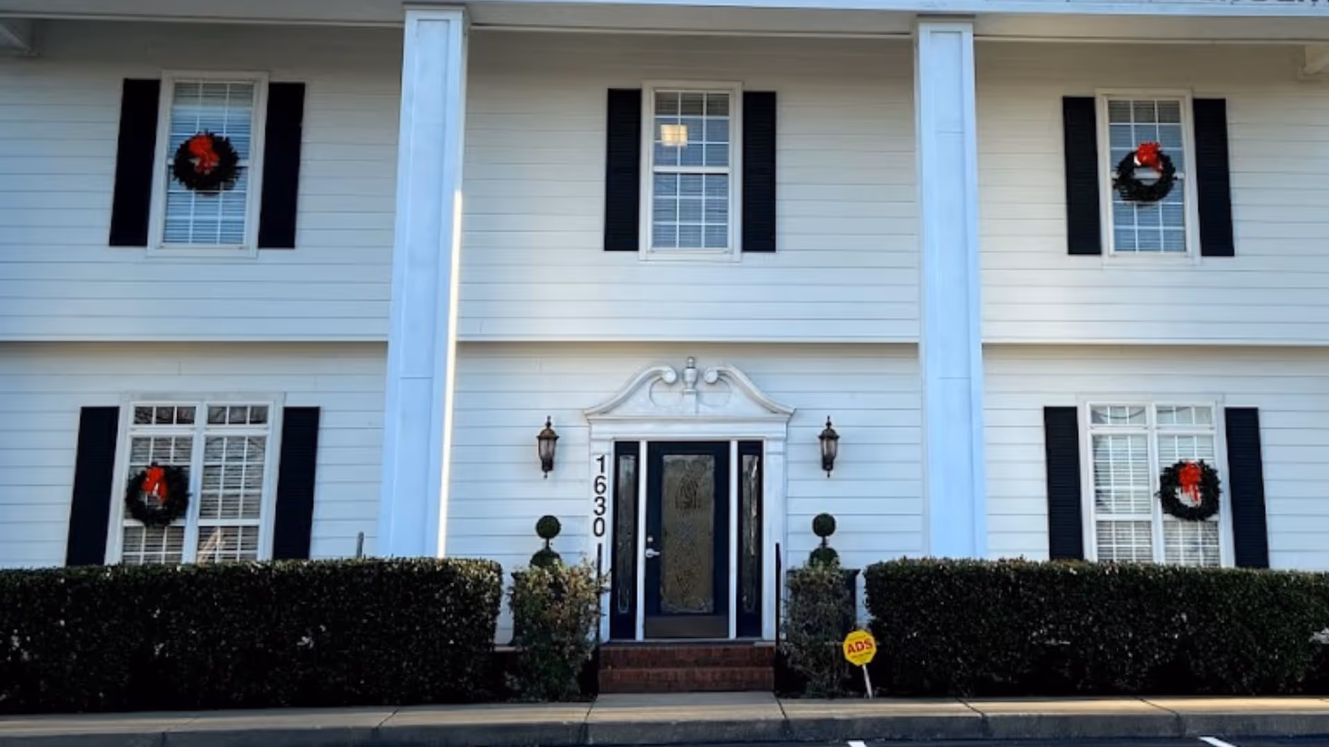 White two-story building front with wreaths, black shutters, and central doorway.