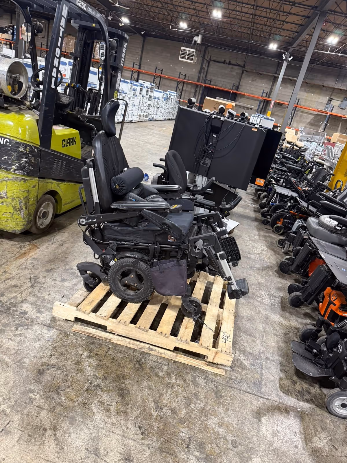 Wheelchair on a wooden pallet in a cluttered warehouse with other equipment