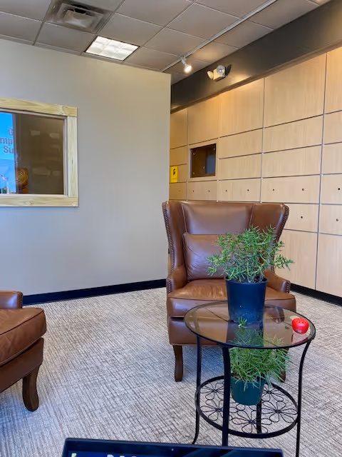 Cozy lobby area with brown leather chairs, glass coffee table, and potted plant.