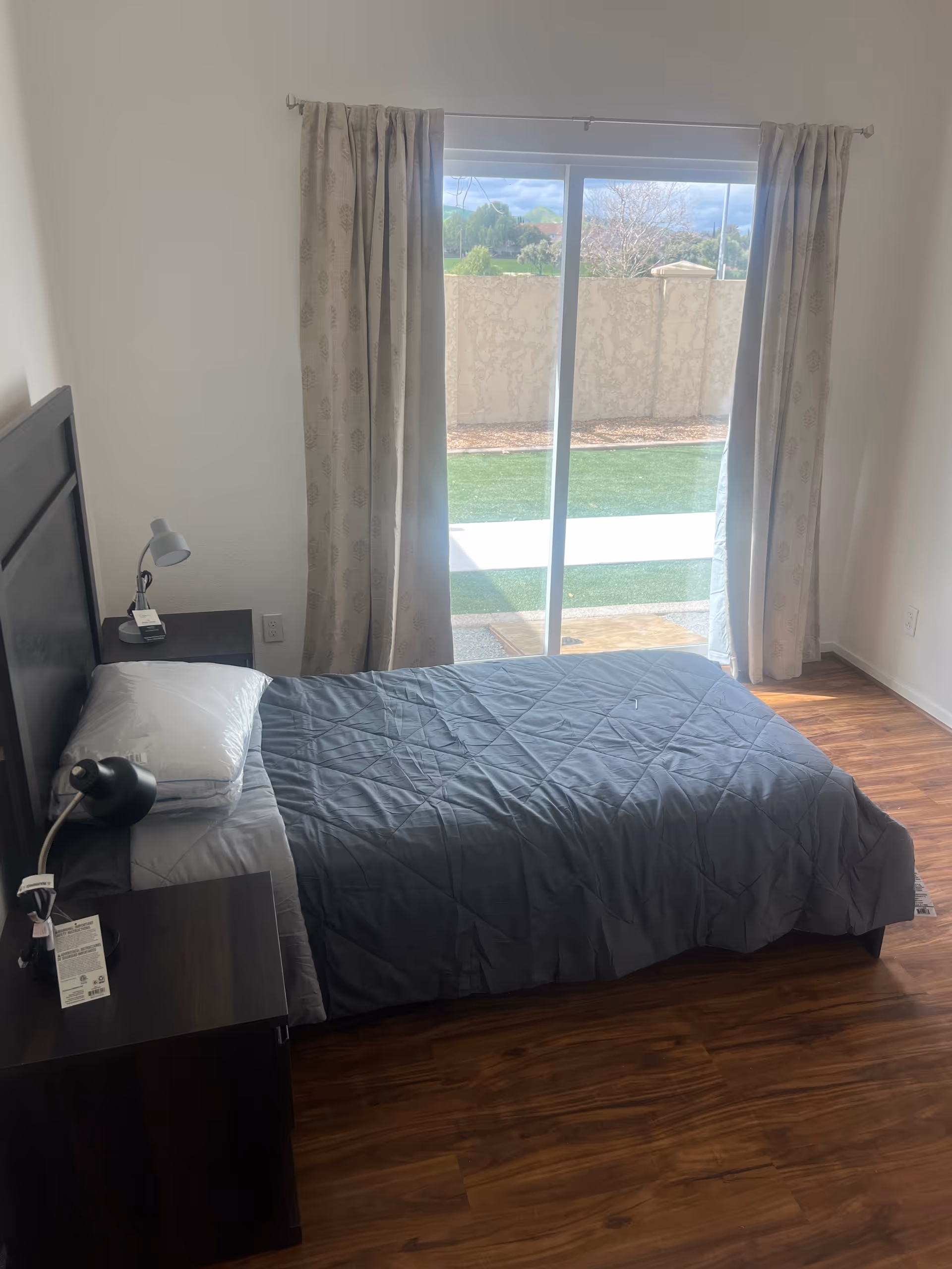 A simple bedroom with a bed, a nightstand, and a sliding glass door to the outdoors.