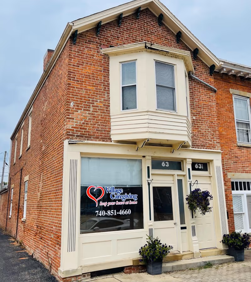 Brick building with Village Caregiving sign in window and potted plants near the entrance.