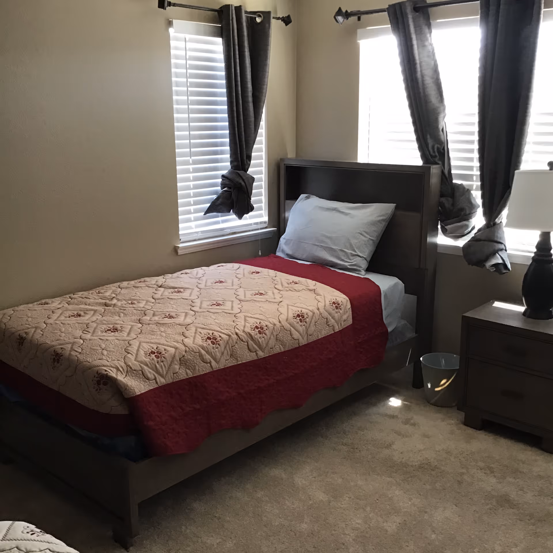 Bedroom featuring a single bed, quilt, bedside table, and two windows.