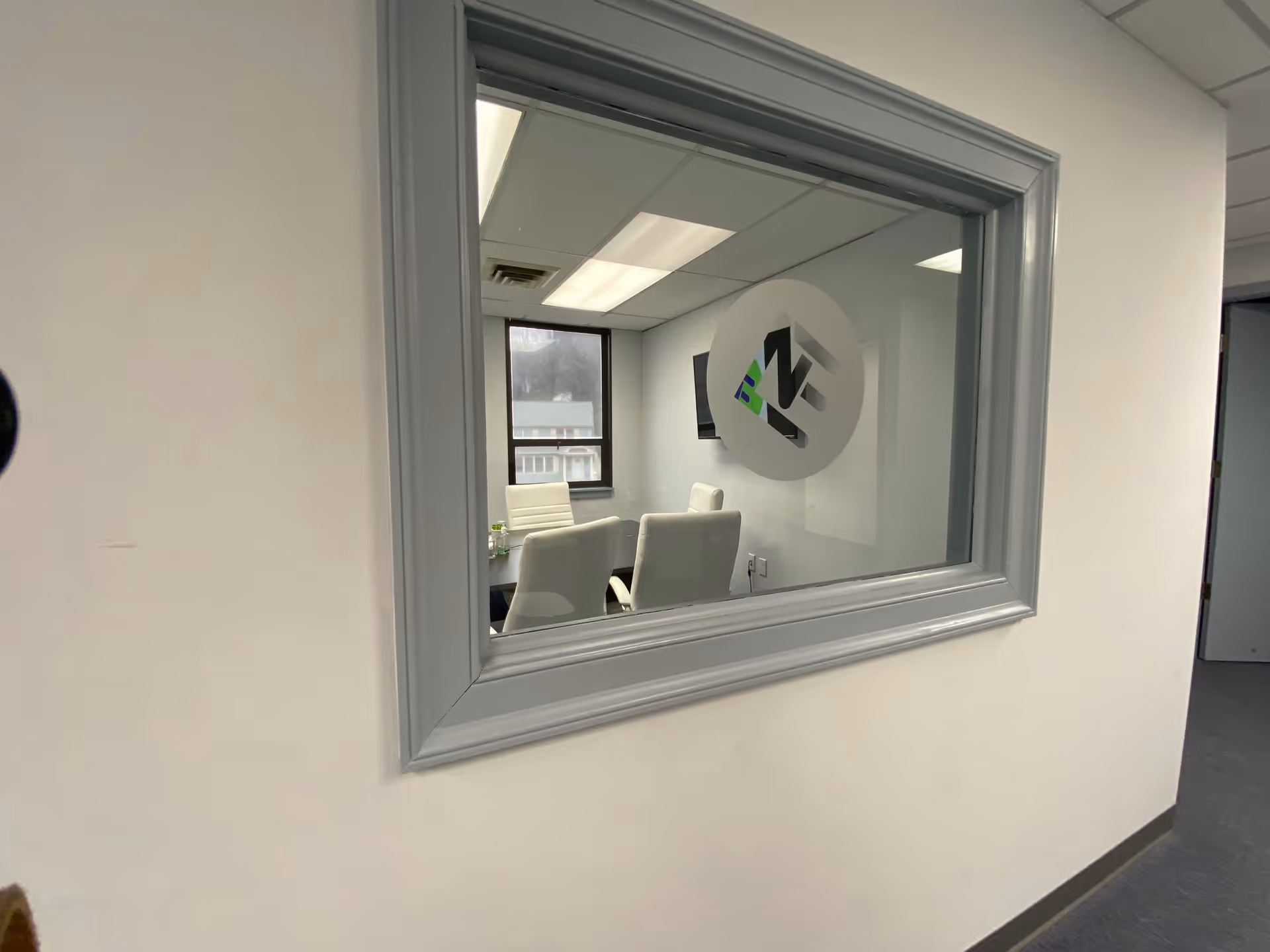 Through a large window, a conference room with white chairs and a round logo on wall.