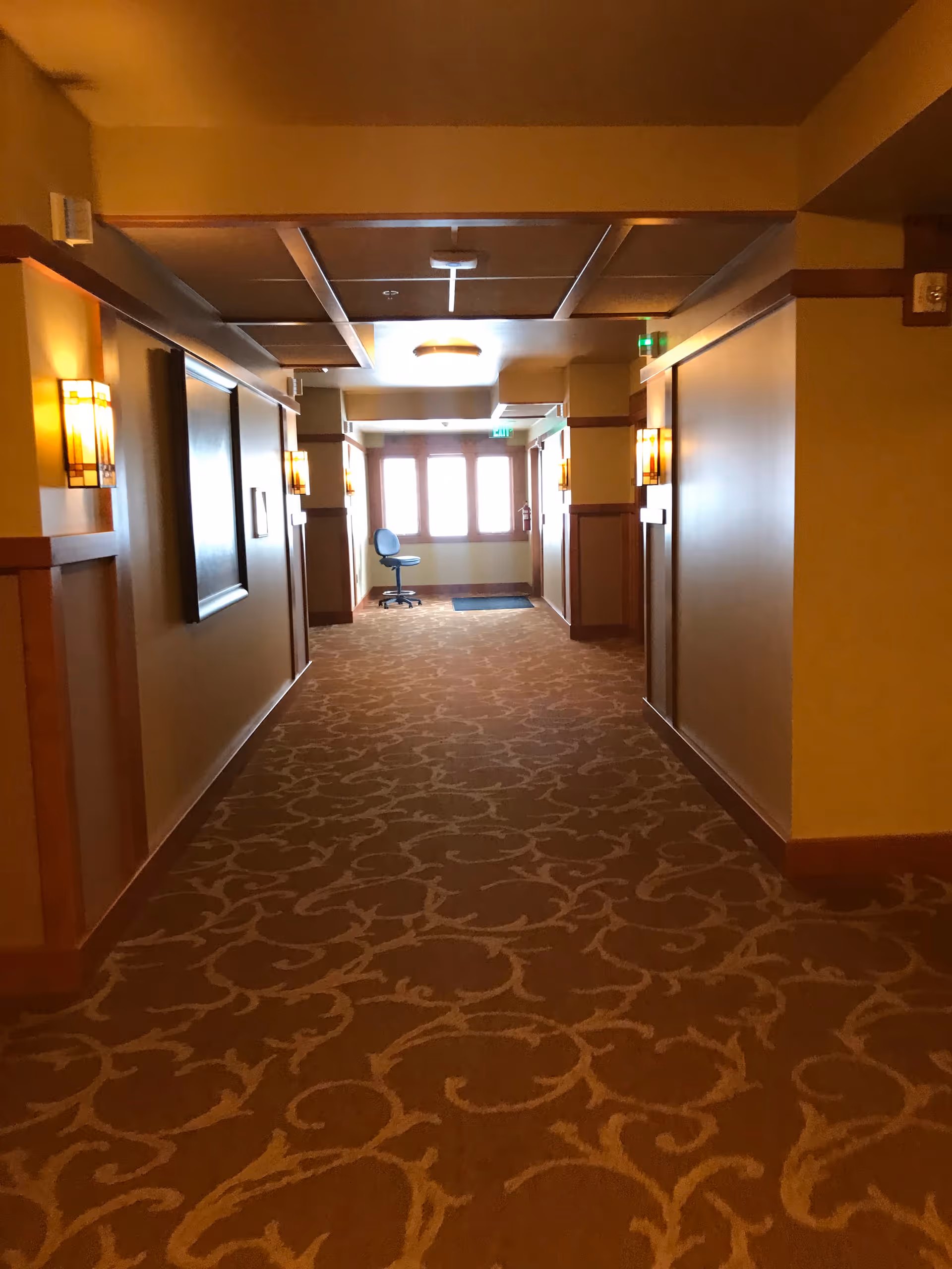 Long corridor in a senior living facility with patterned carpet and warm wall lighting.