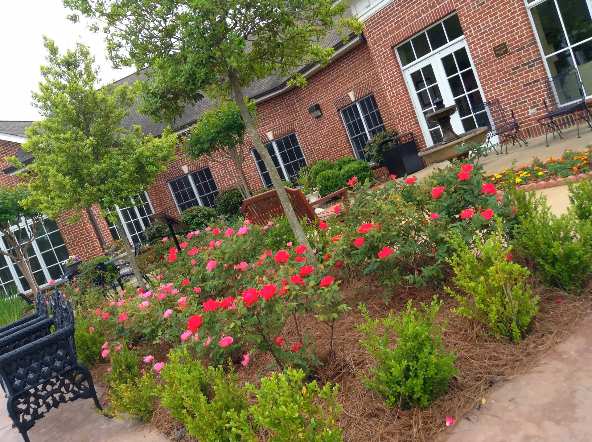 Brick building with a rose-filled courtyard, trees, and outdoor seating.