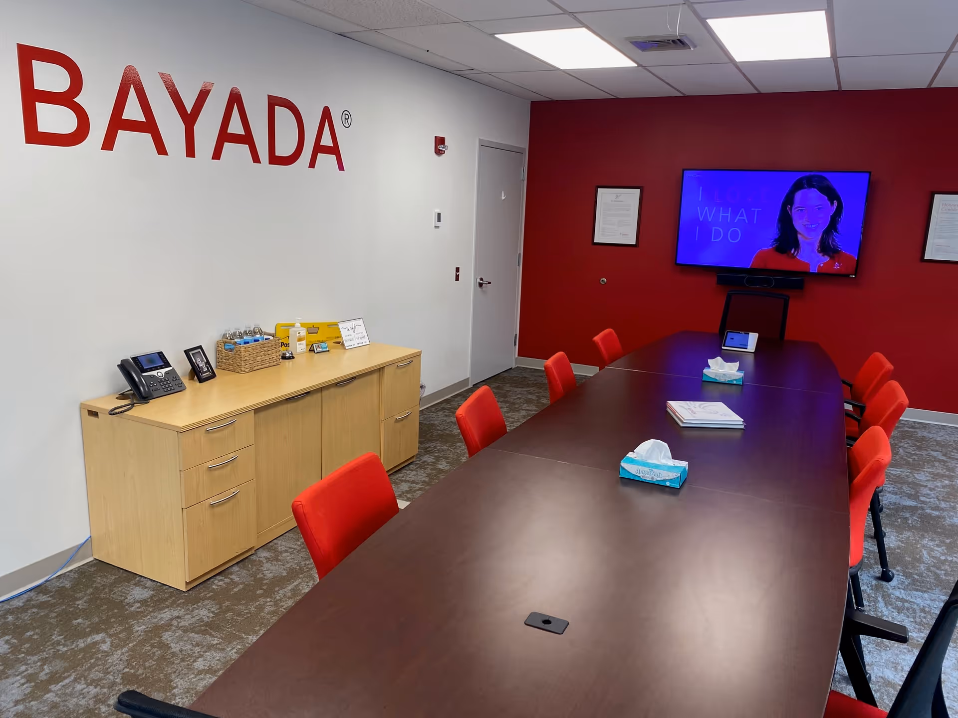 A conference room with a long table, red chairs, and a BAYADA sign on the wall.