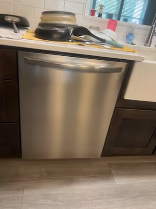 Stainless dishwasher under a kitchen counter with dishes and cleaning items