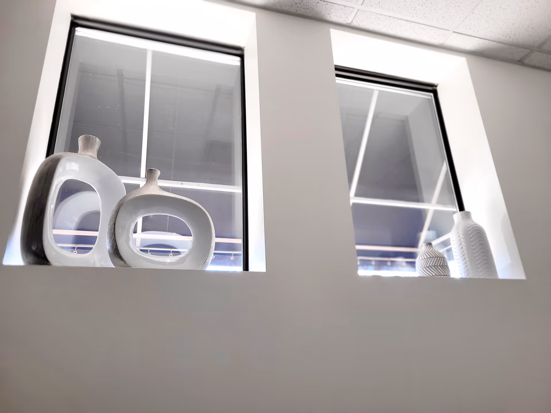 Two windows with white decorative vases on a ledge inside a modern interior.