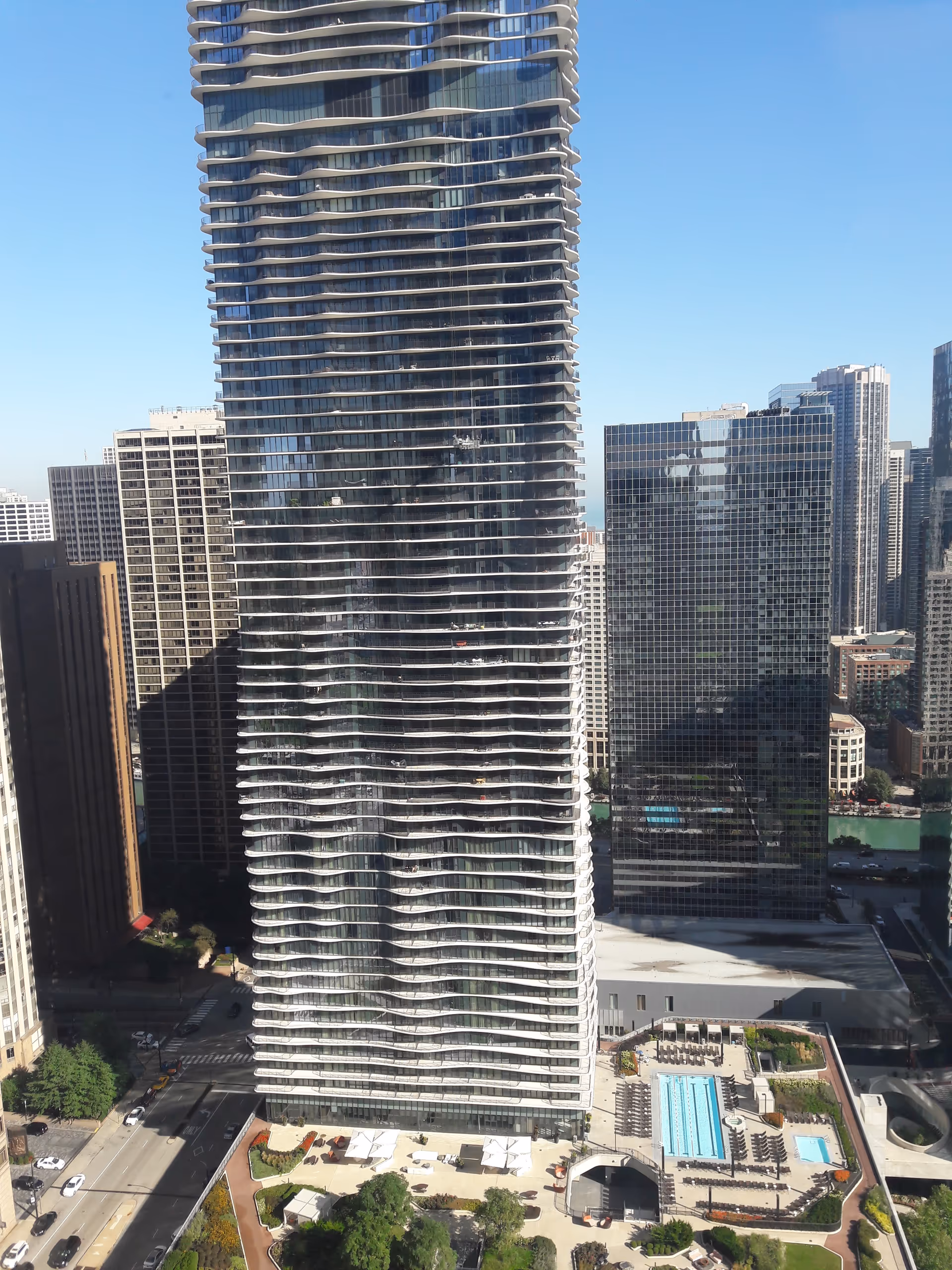 A tall glass skyscraper dominates a downtown skyline with a visible outdoor pool area.