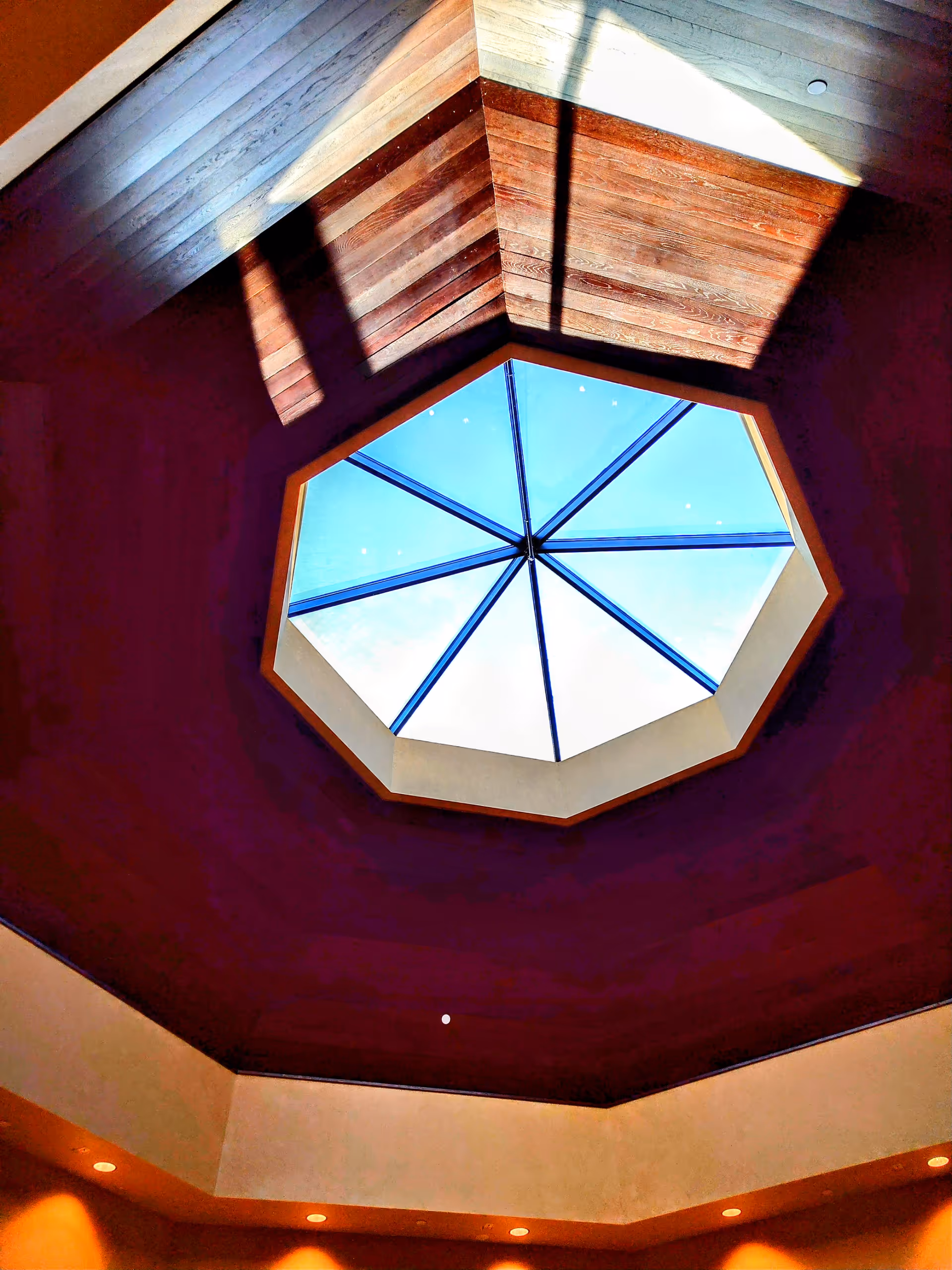 Octagonal skylight in a wood-paneled atrium ceiling, blue sky visible through glass panes.