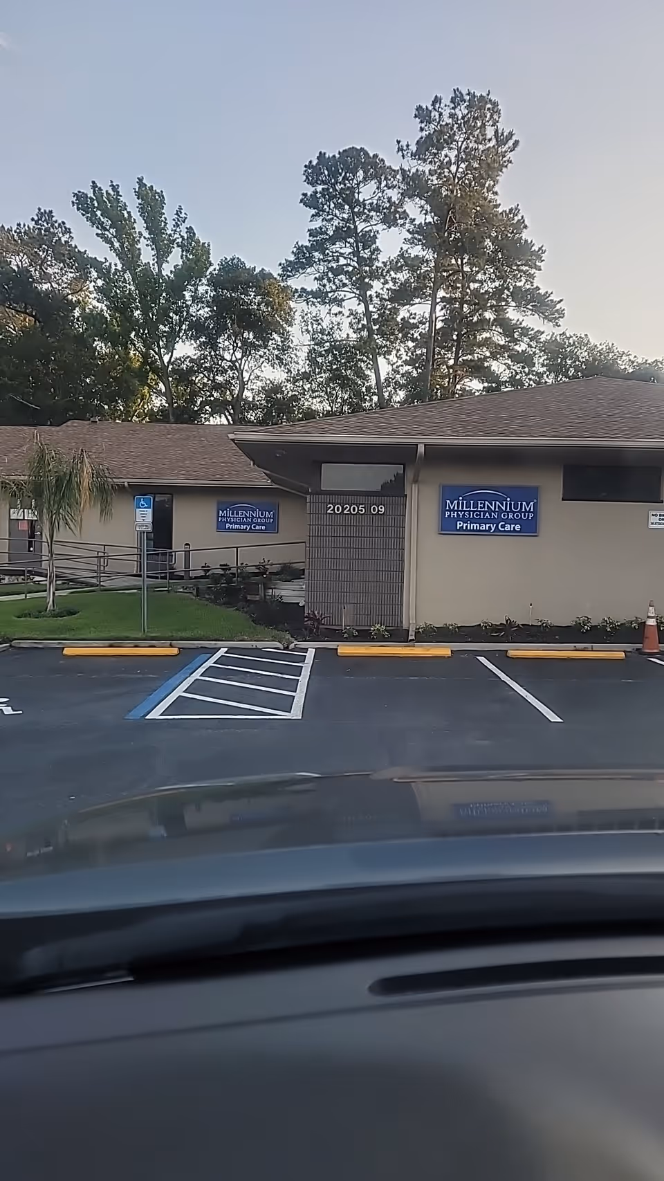 Front exterior of a beige medical building with blue Millennium Physician Group signs and parking.