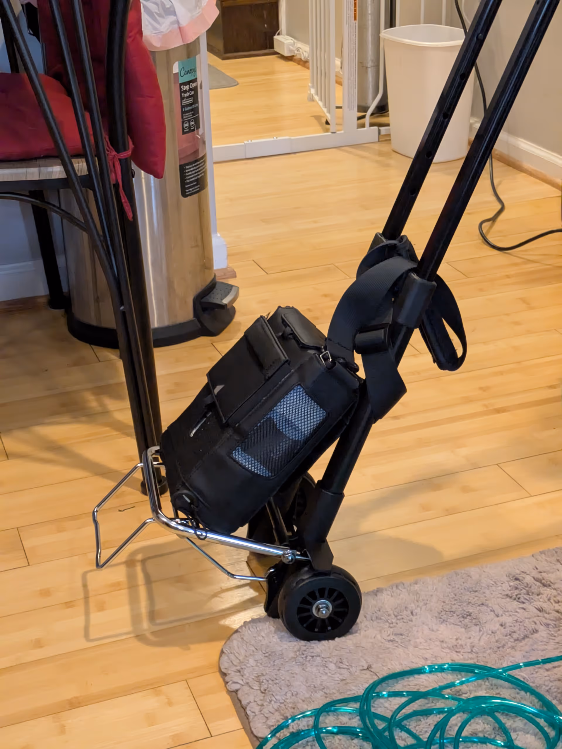 A black wheeled mobility device sits on a light wooden floor indoors.