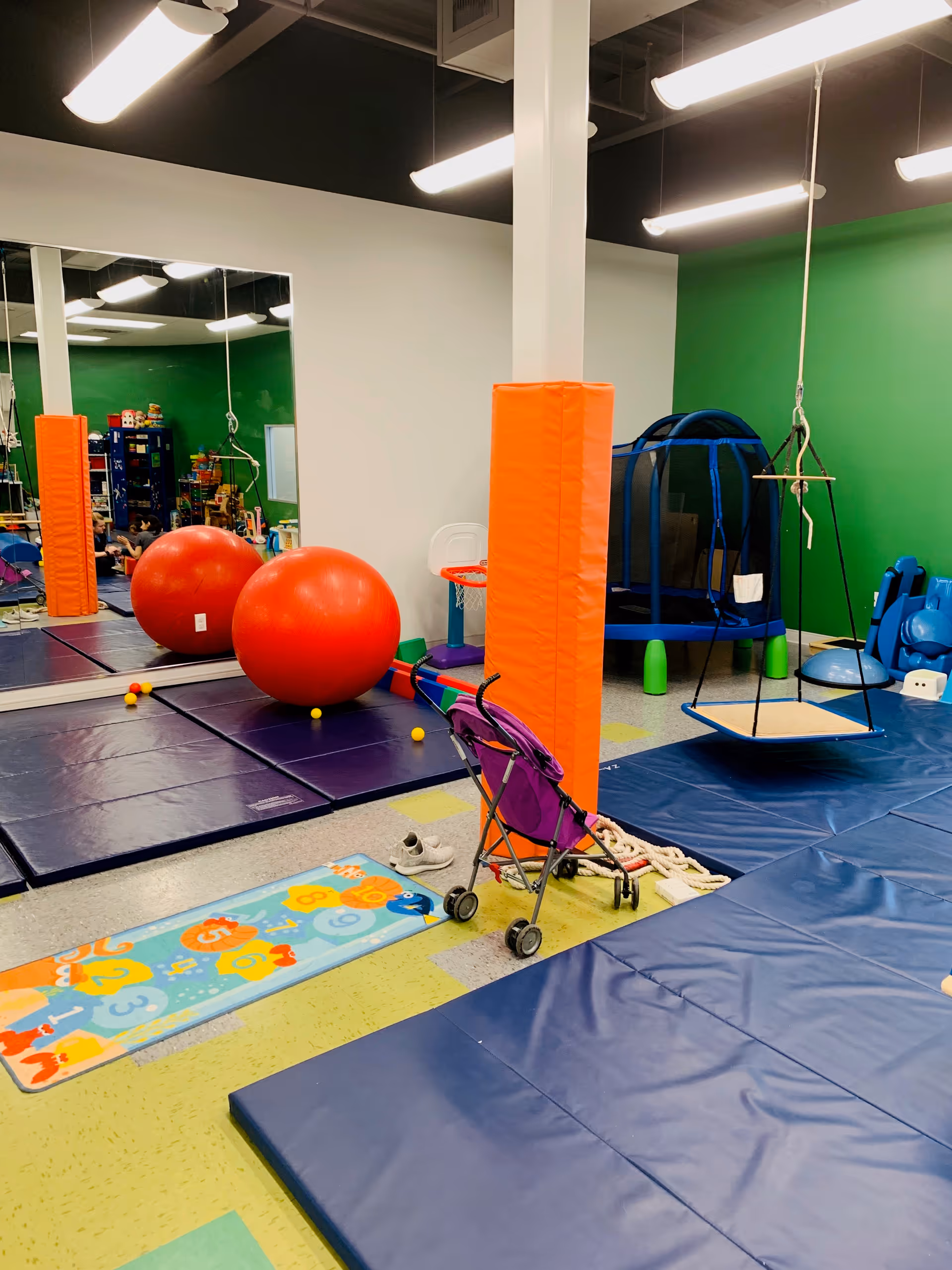 Indoor pediatric therapy playroom with padded mats, large red exercise balls, and climbing equipment.