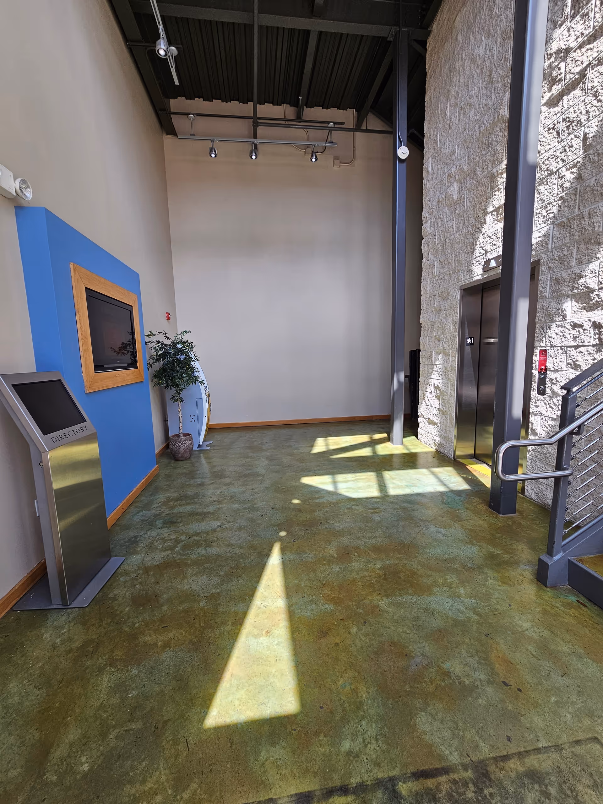 Lobby-like interior with elevator, staircase, blue accent wall, and a potted plant.