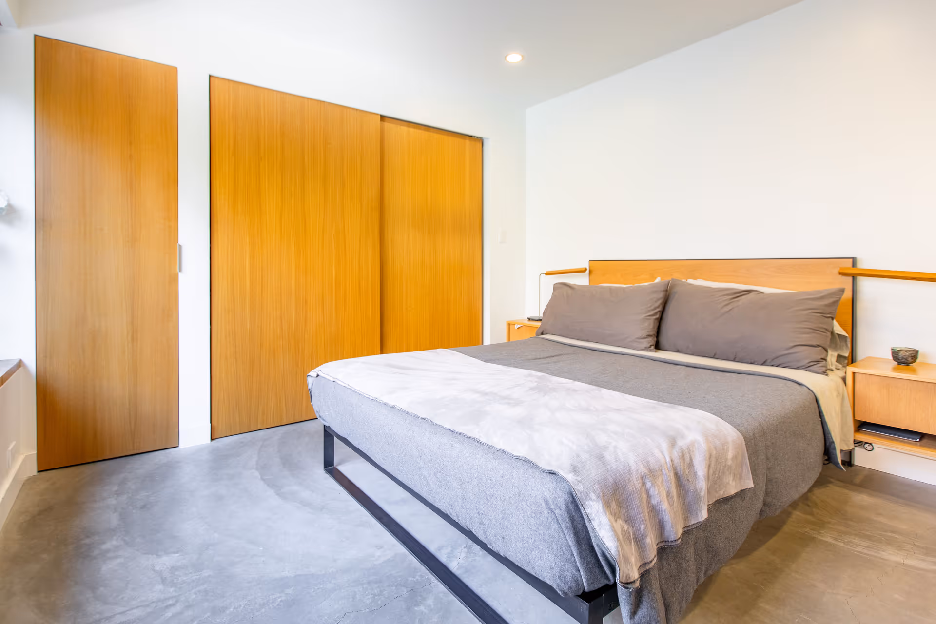 Modern bedroom with a low-profile bed, gray bedding, and wooden wardrobes.