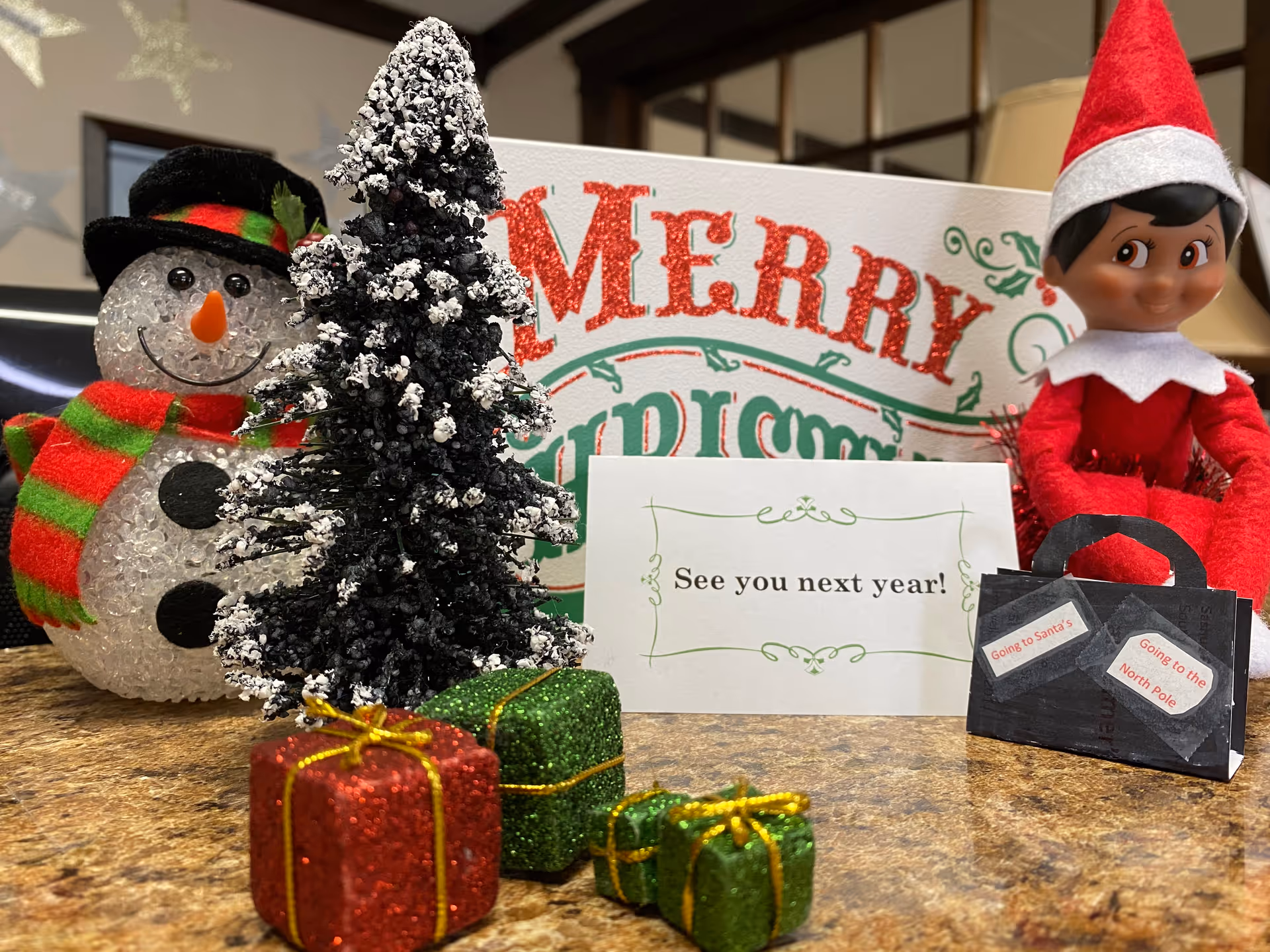 Festive holiday display at a Comfort Keepers facility, featuring snowman, elf figure, tree, and gifts.