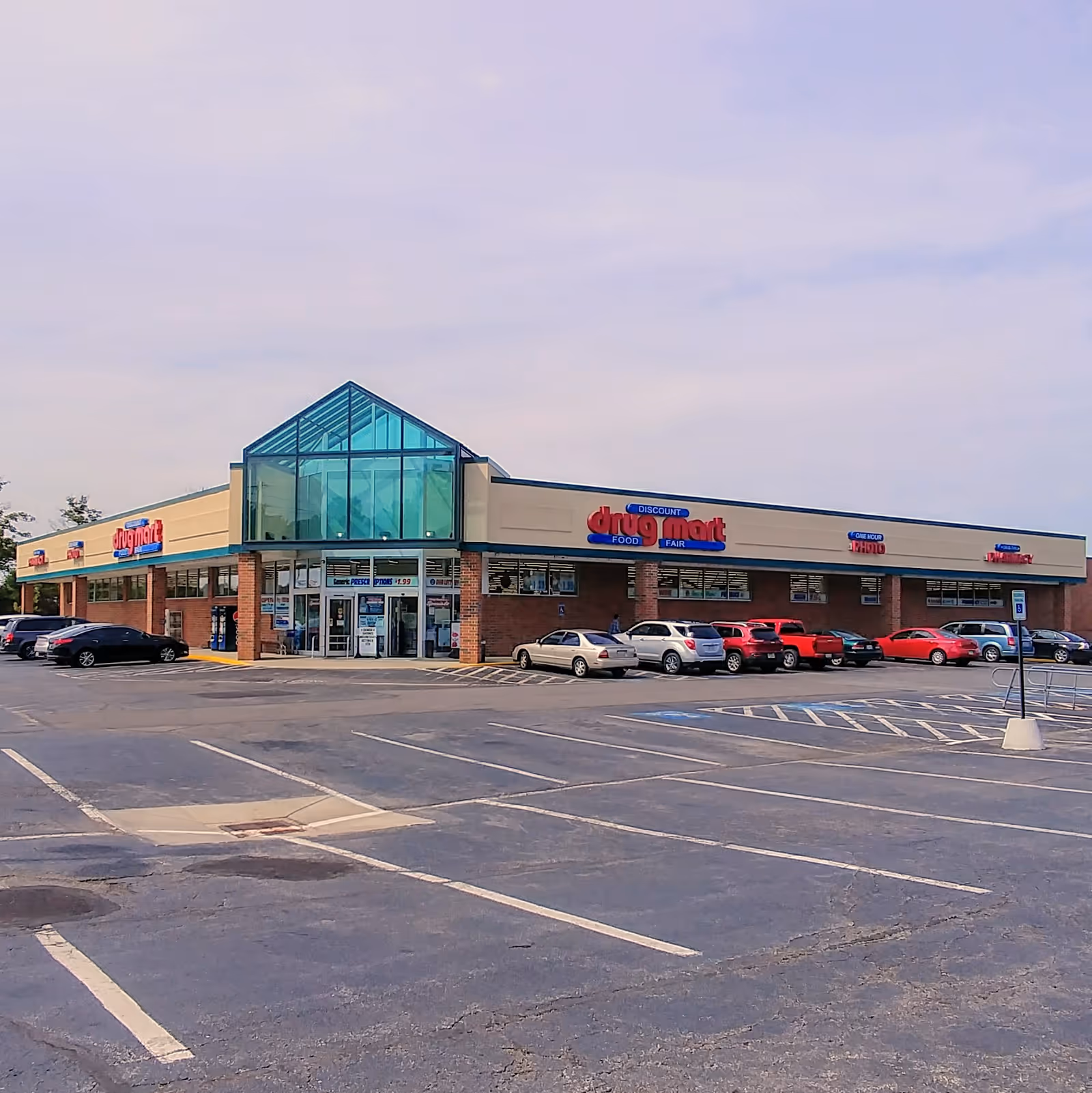 Exterior view of Discount Drug Mart storefront with a large green glass roof and parking lot.