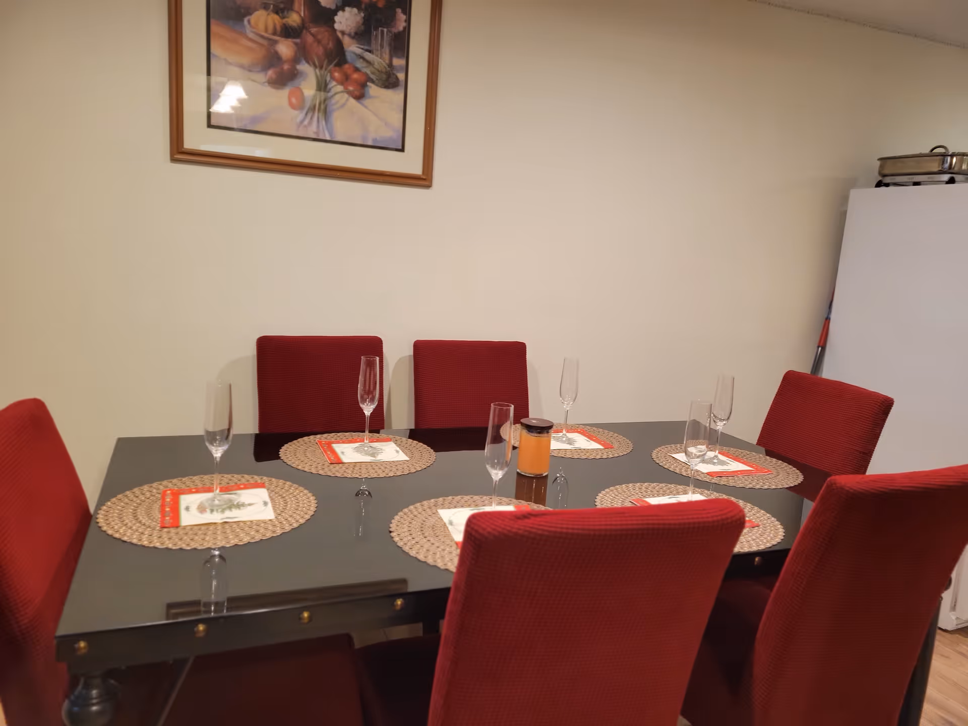 Red upholstered dining chairs surround a glass table set with placemats and glasses.