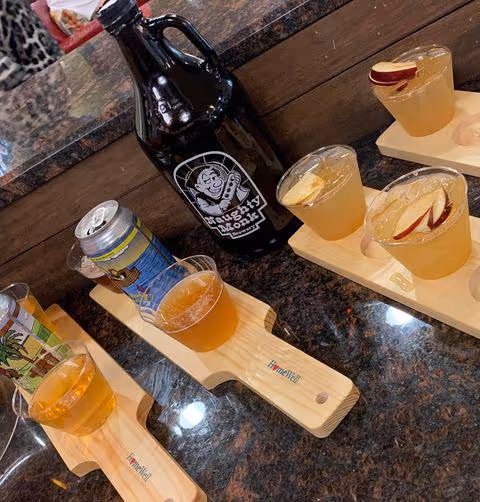 Wooden beer flight paddles with small glasses sit beside a dark bottle on a granite bar.