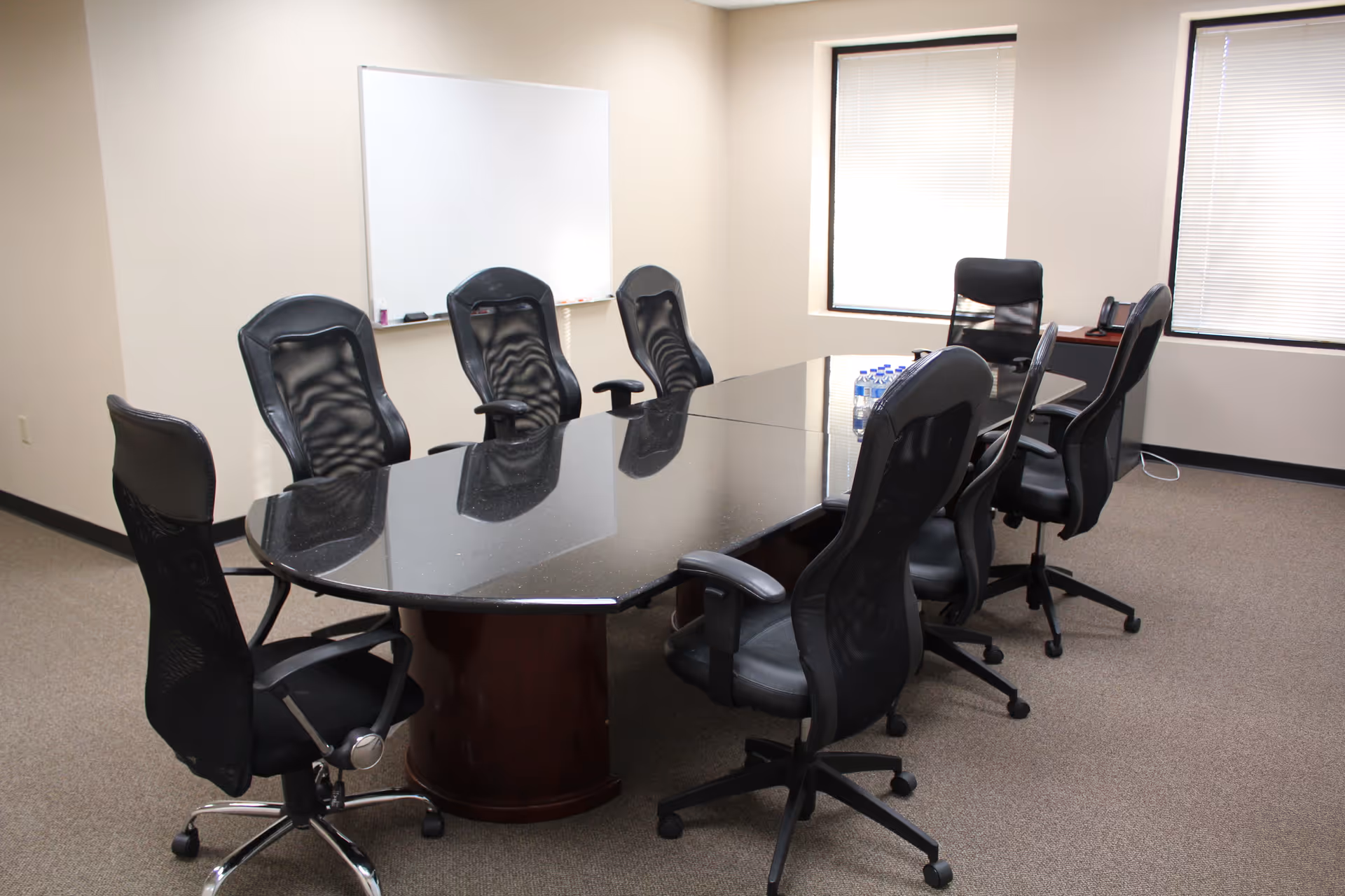 A spacious conference room with a glass-topped oval table and black office chairs.