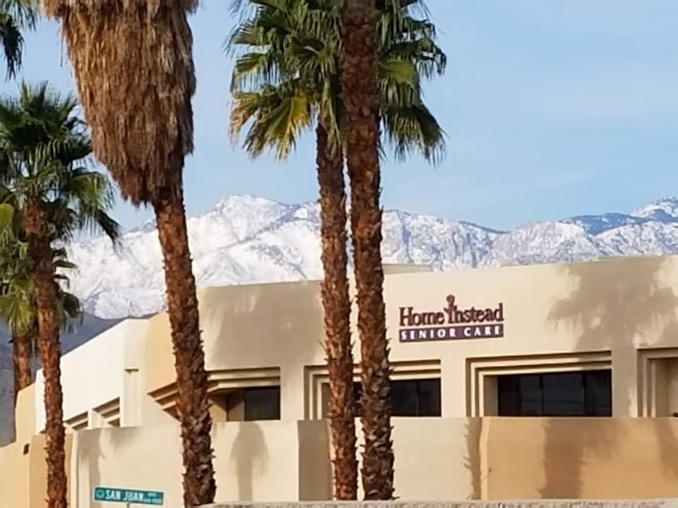Exterior view of Home Instead Senior Care building with palm trees and snowy mountains behind.
