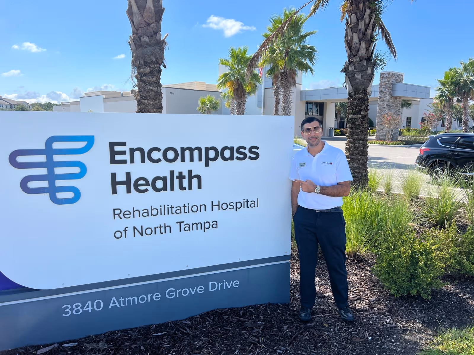 Man in a white polo stands beside the Encompass Health sign at the Rehabilitation Hospital entrance