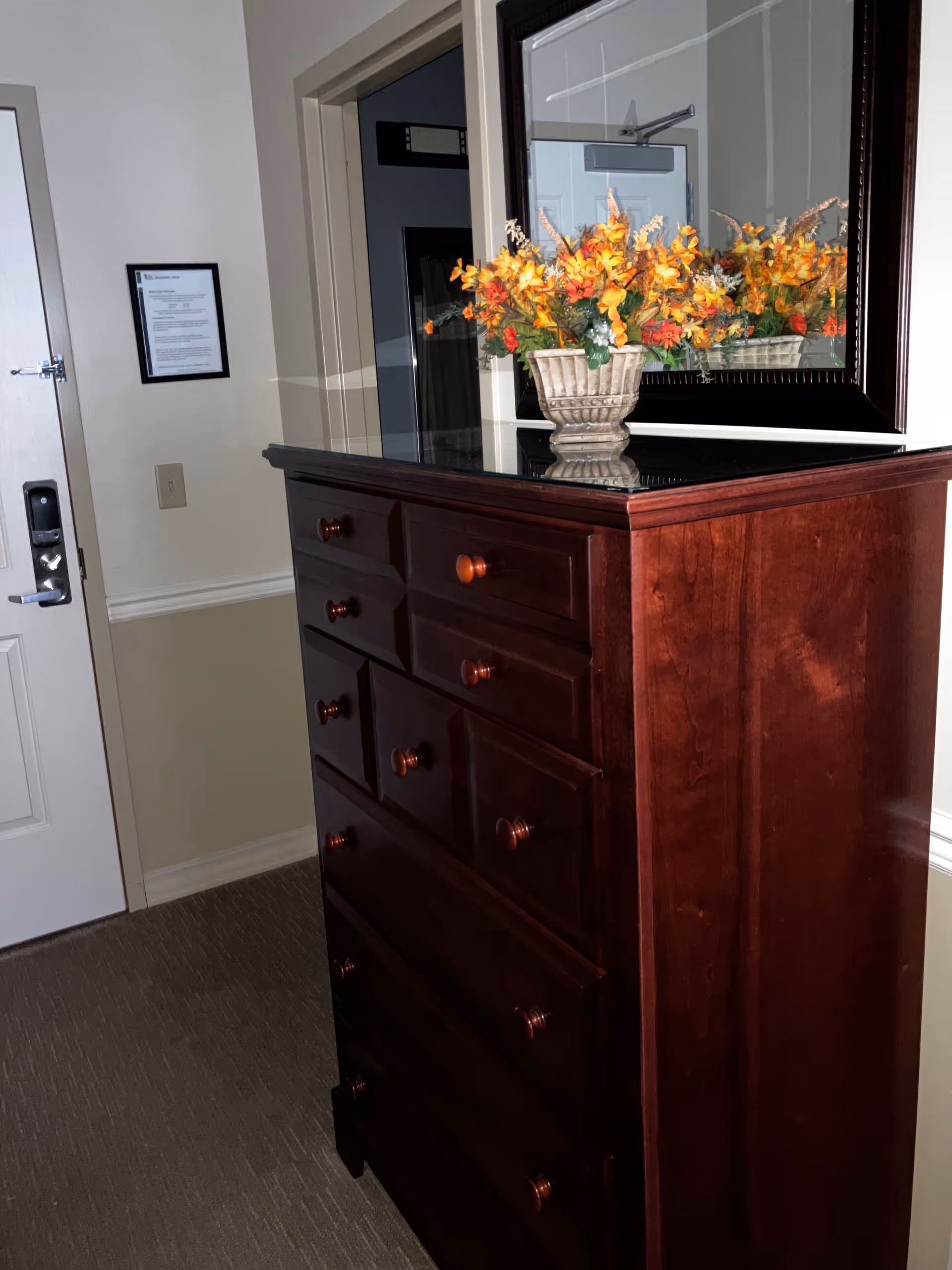 A dark wooden dresser with a floral arrangement stands in a hallway beside a door.