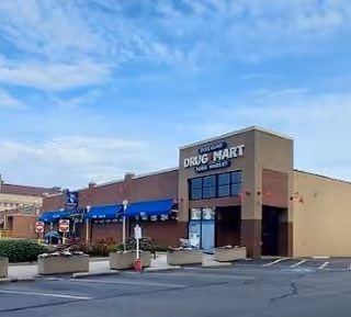 Exterior view of Discount Drug Mart storefront with blue awnings and parking lot.