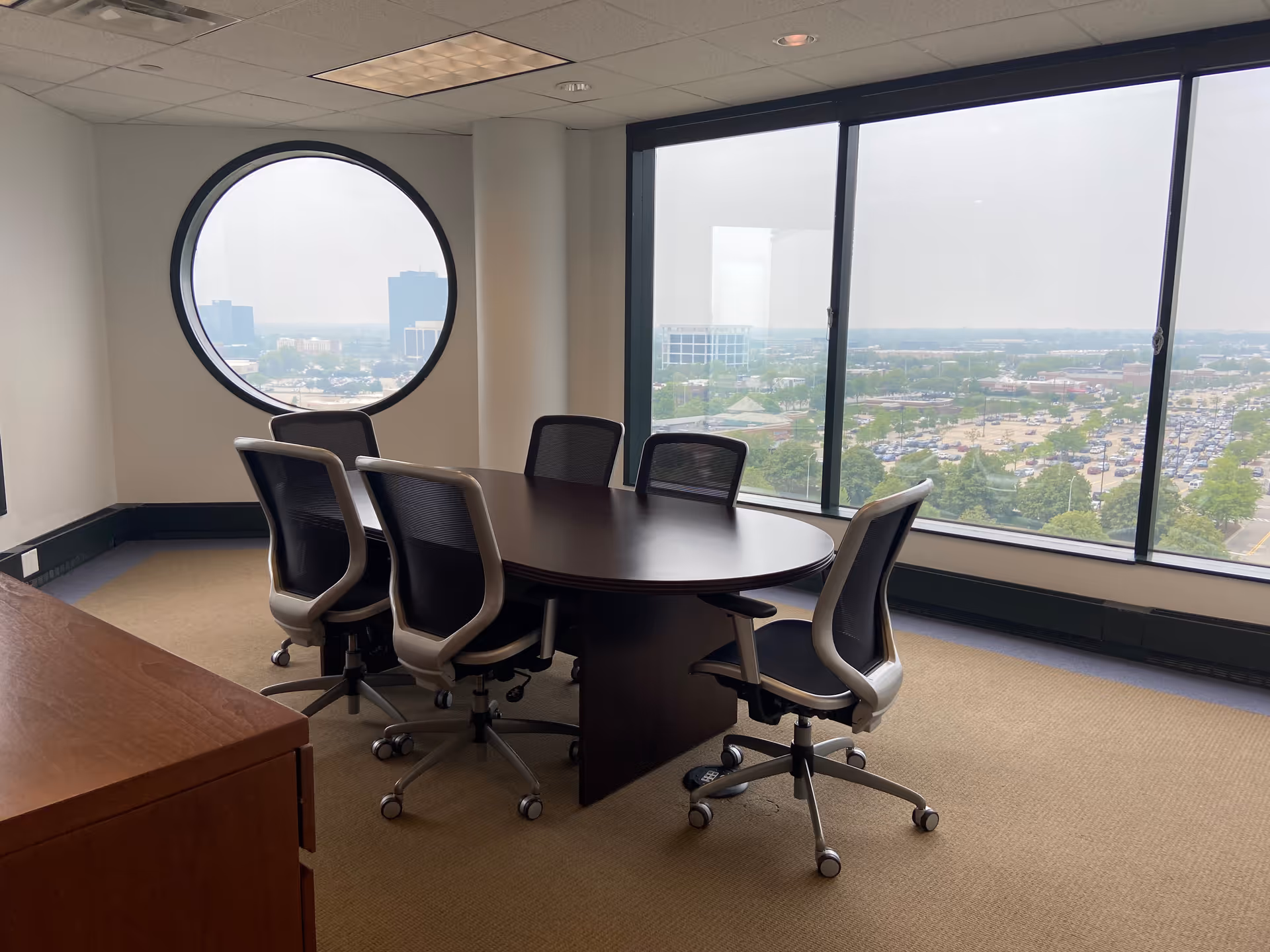 Round conference table with chairs in a bright office meeting room by large windows.