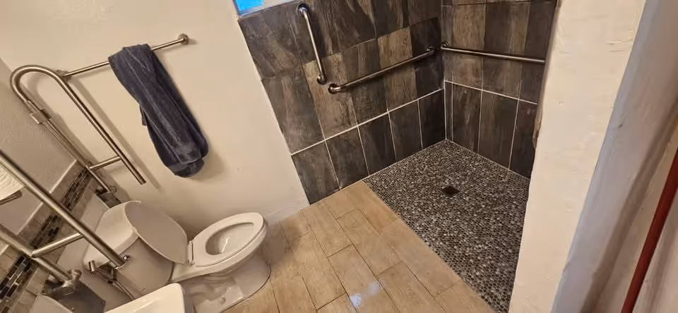Compact bathroom with toilet, towel, and accessible shower featuring safety grab bars.