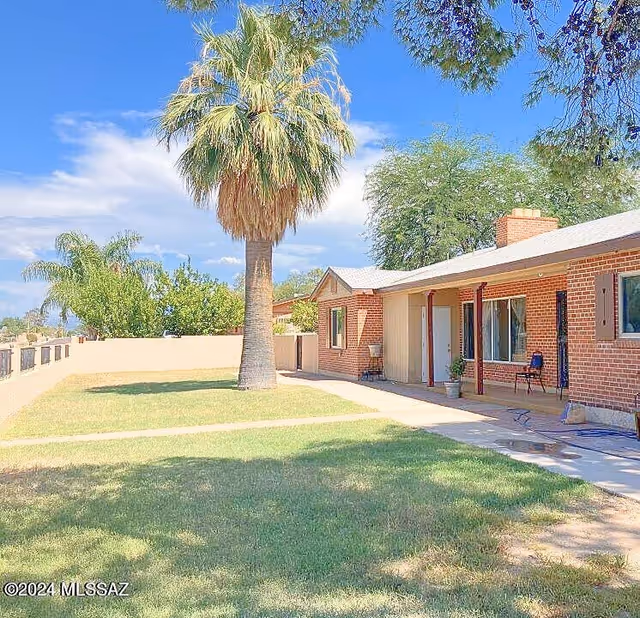 Single-story brick facility with a lawn, patio, and large palm tree.