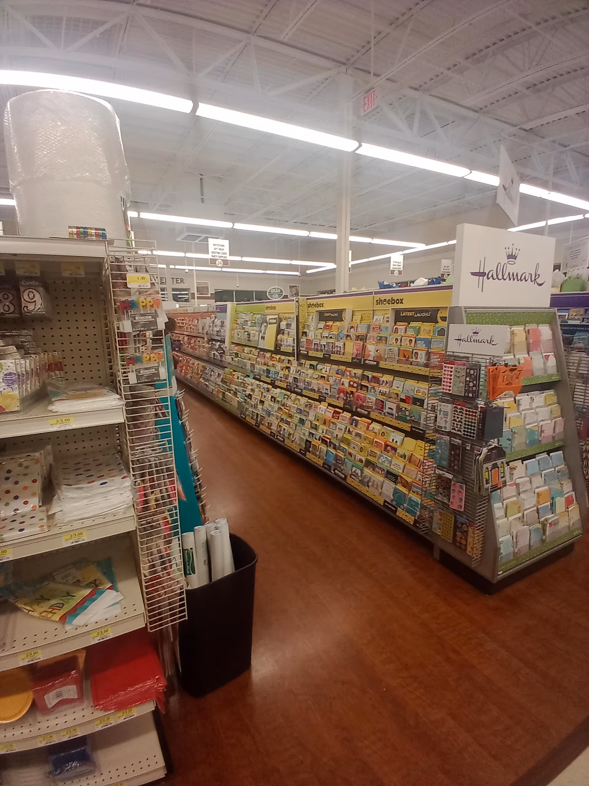 A store aisle lined with greeting cards and Hallmark displays in a drugstore.