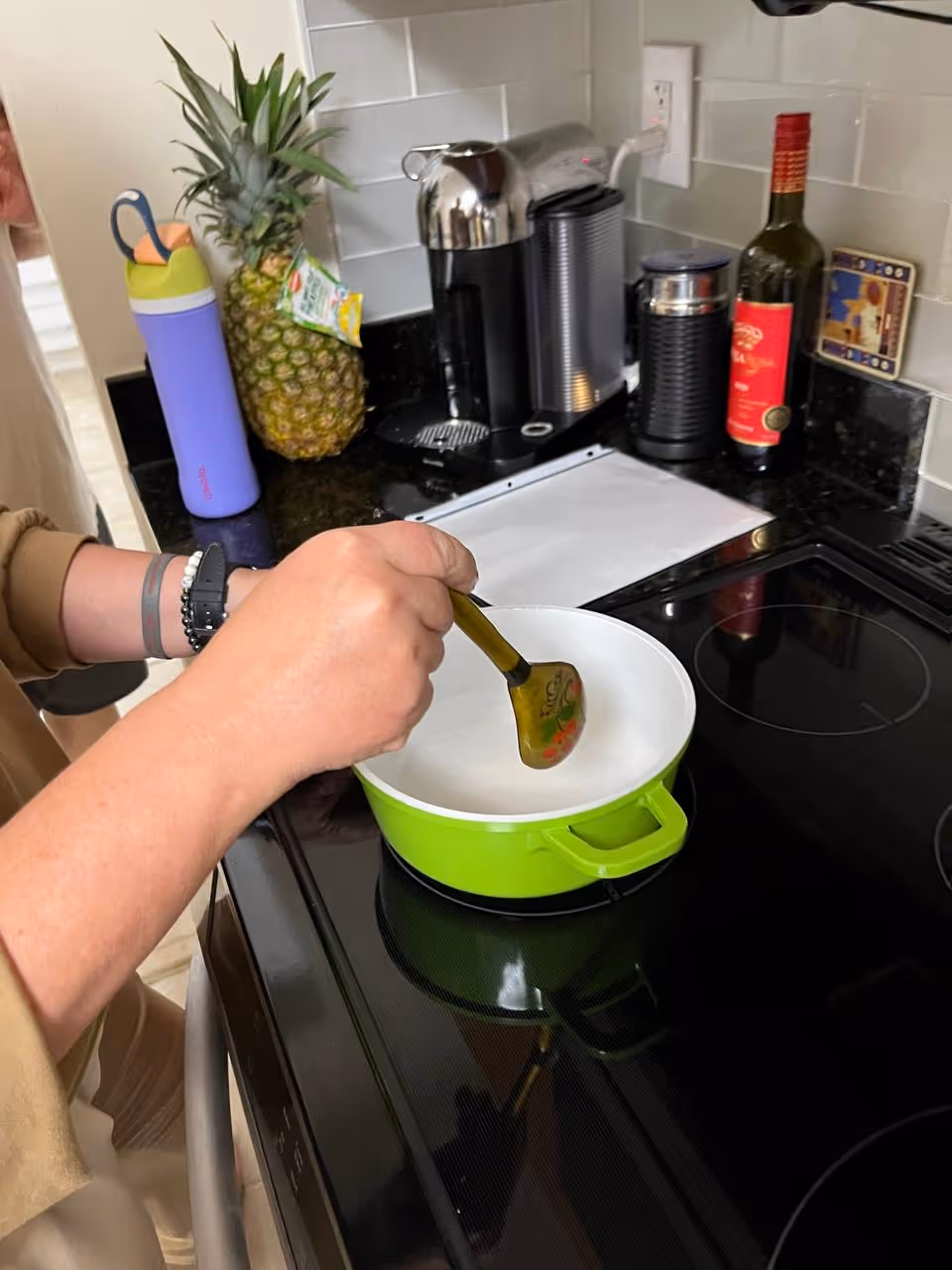Person stirs a green pot on a black stovetop in a modern kitchen.