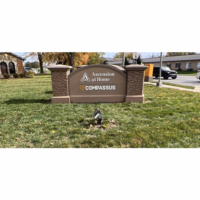 Outdoor sign with stone pillars reading Ascension at Home Compassus on a grassy front yard.