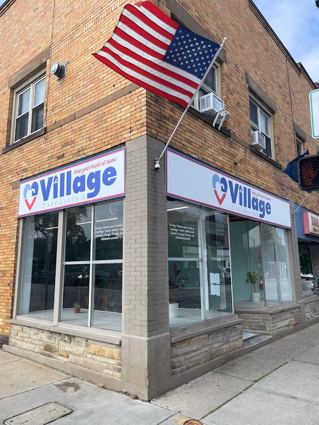 Brick corner building with Village Caregiving storefront signs and an American flag.