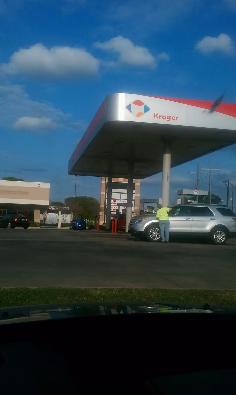 Kroger gas station canopy with a person near a silver SUV under blue sky