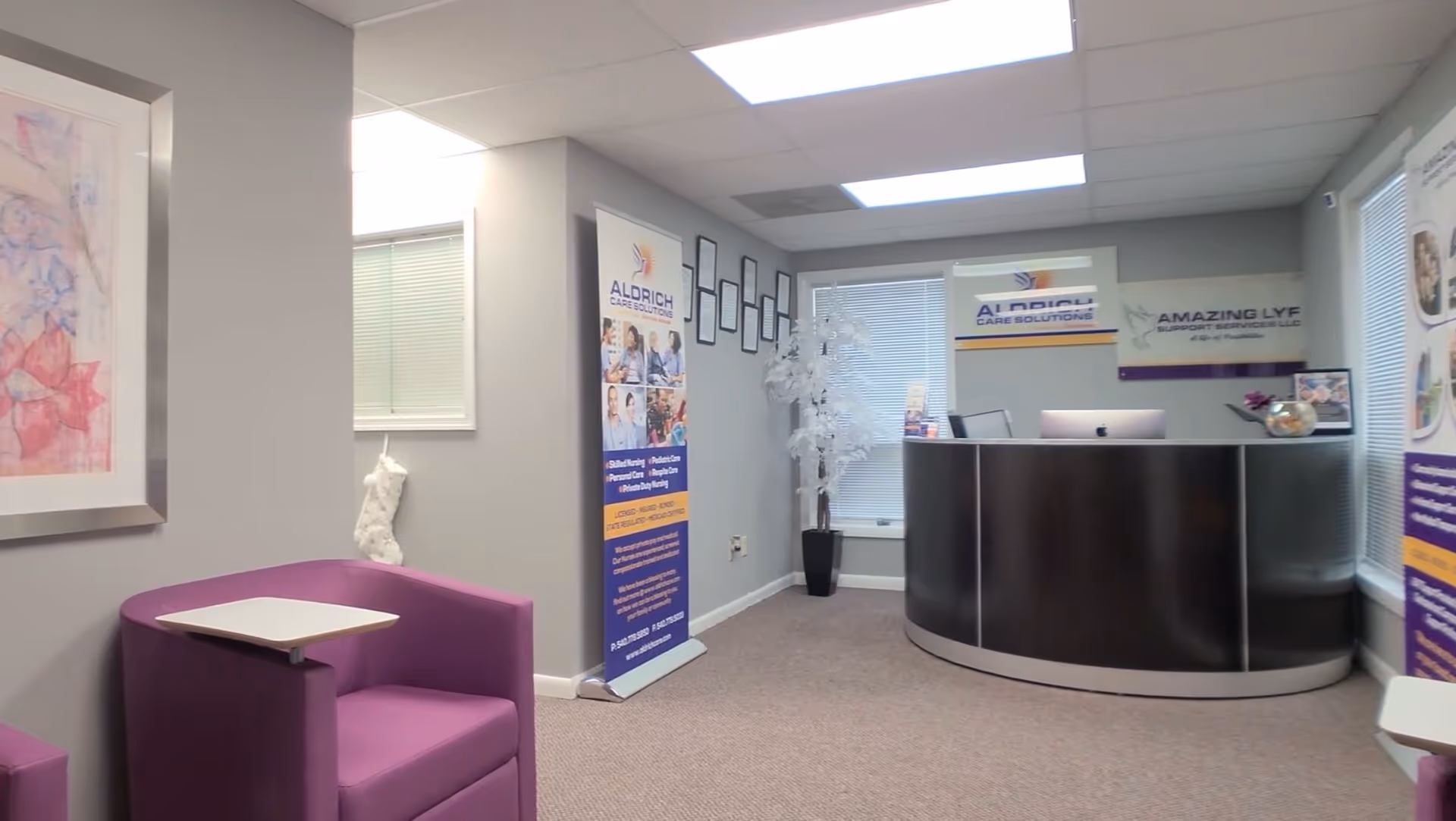 Reception area with curved dark desk, purple seating, and Aldrich Care Solutions banners.