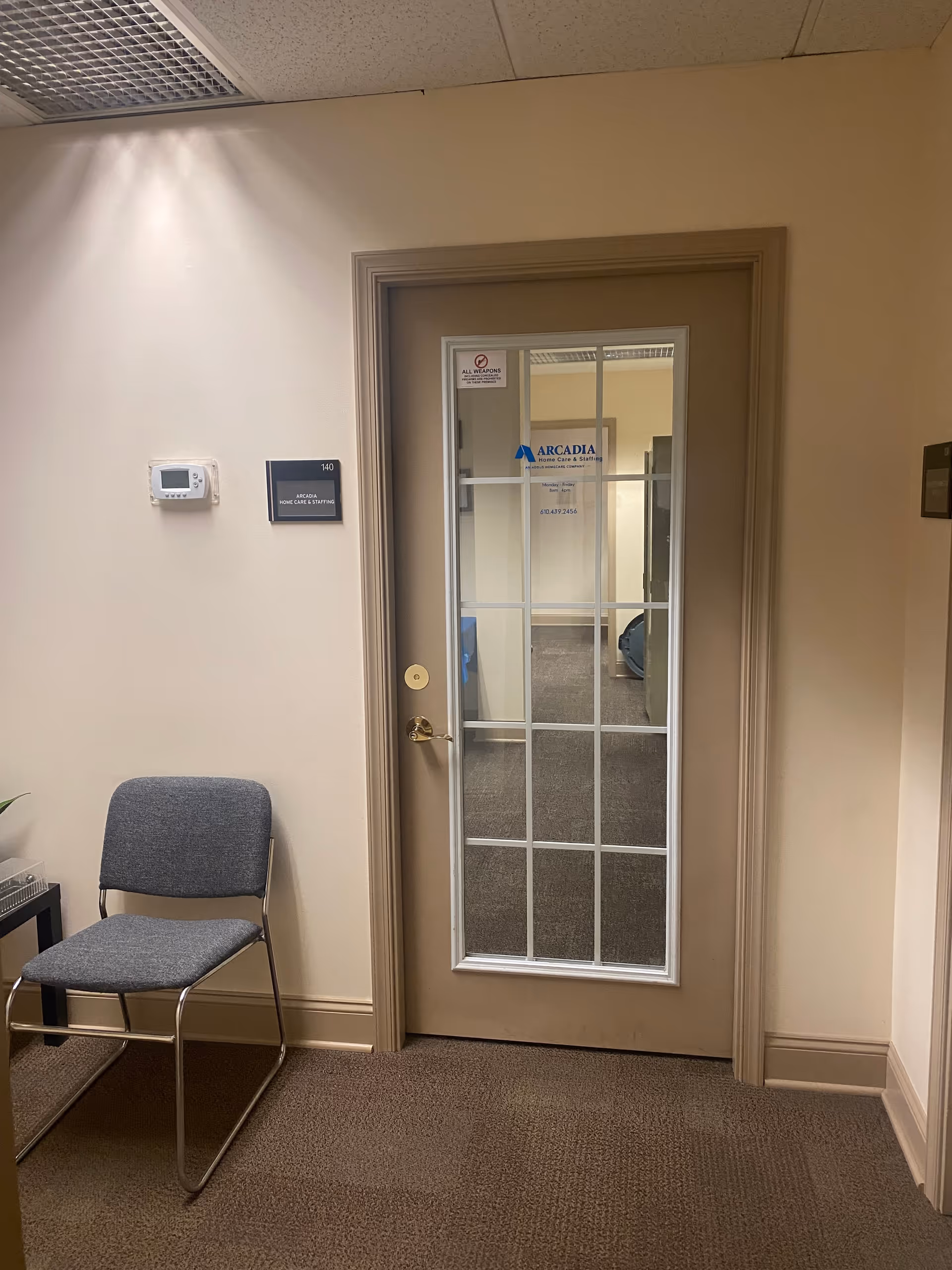 Interior hallway with a glass-paneled door labeled Arcadia, a chair, and a thermostat on the wall.