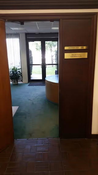 Wooden doorway opens to a lobby with curved reception desk and glass doors.