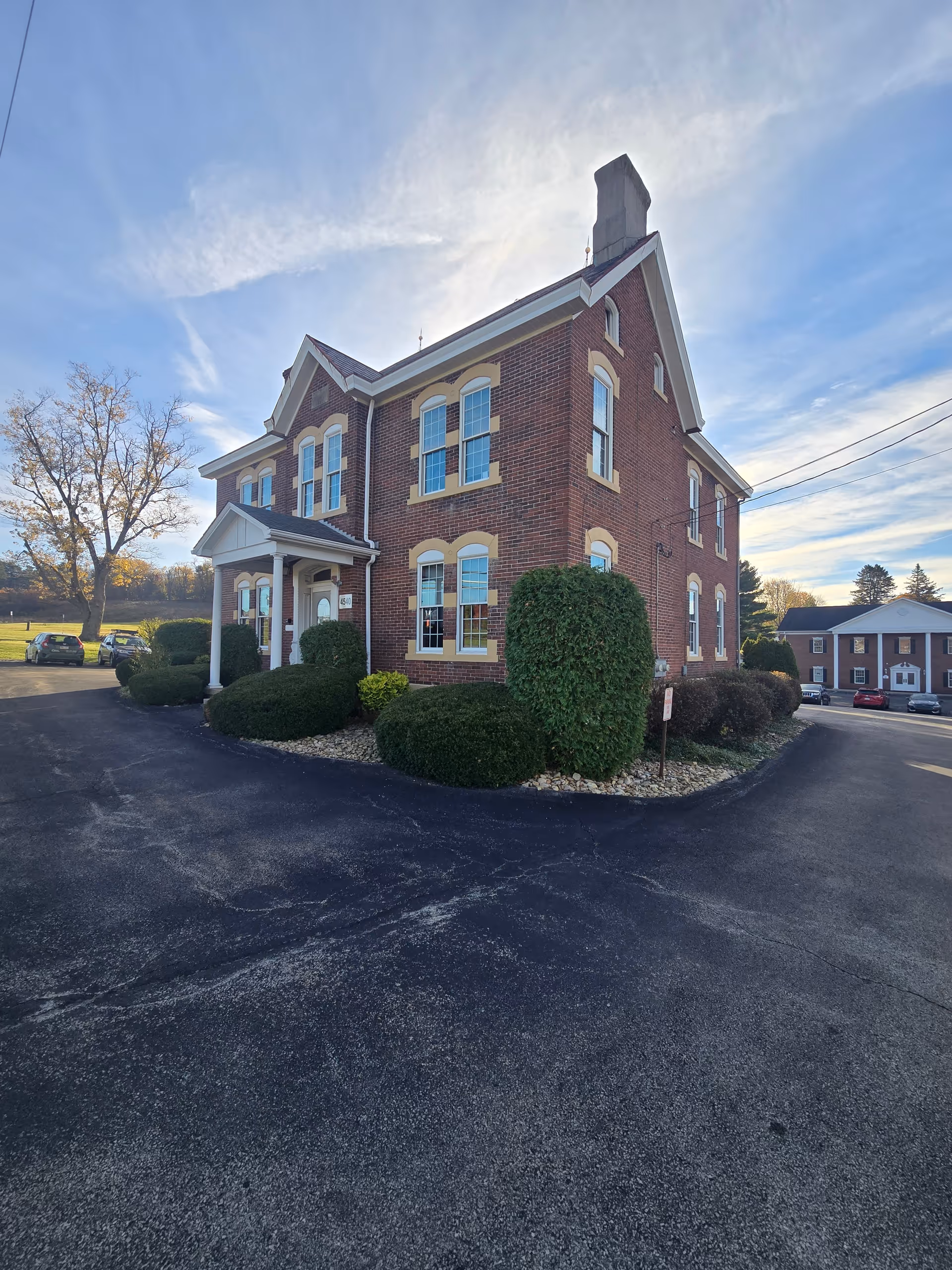 Brick two-story building with arched windows, white trim, and manicured shrubs beside a circular driveway.